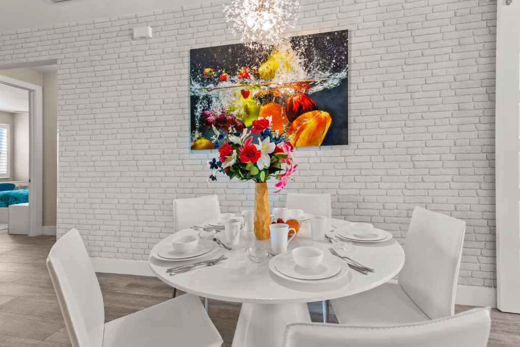 Dining area at Villa Dandelion with round white table, floral centerpiece, and fruit splash wall art.