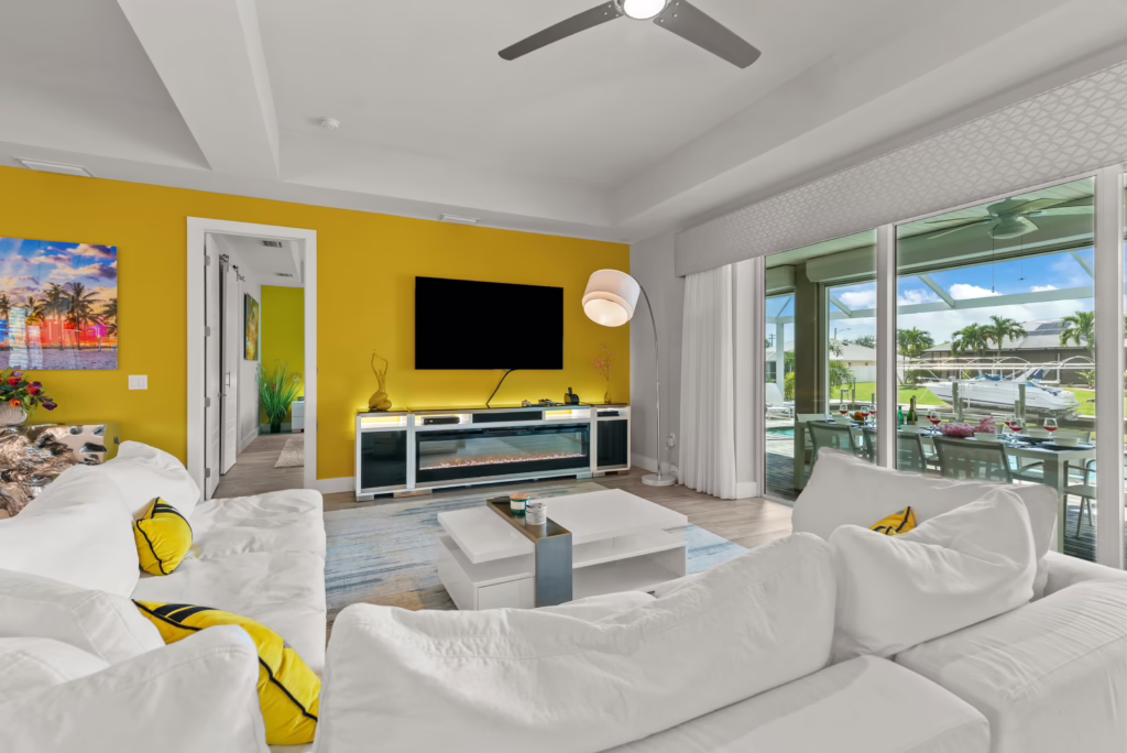 Villa Dandelion living room with white sofa, yellow accent wall, TV, fireplace, and view to terrace and canal.